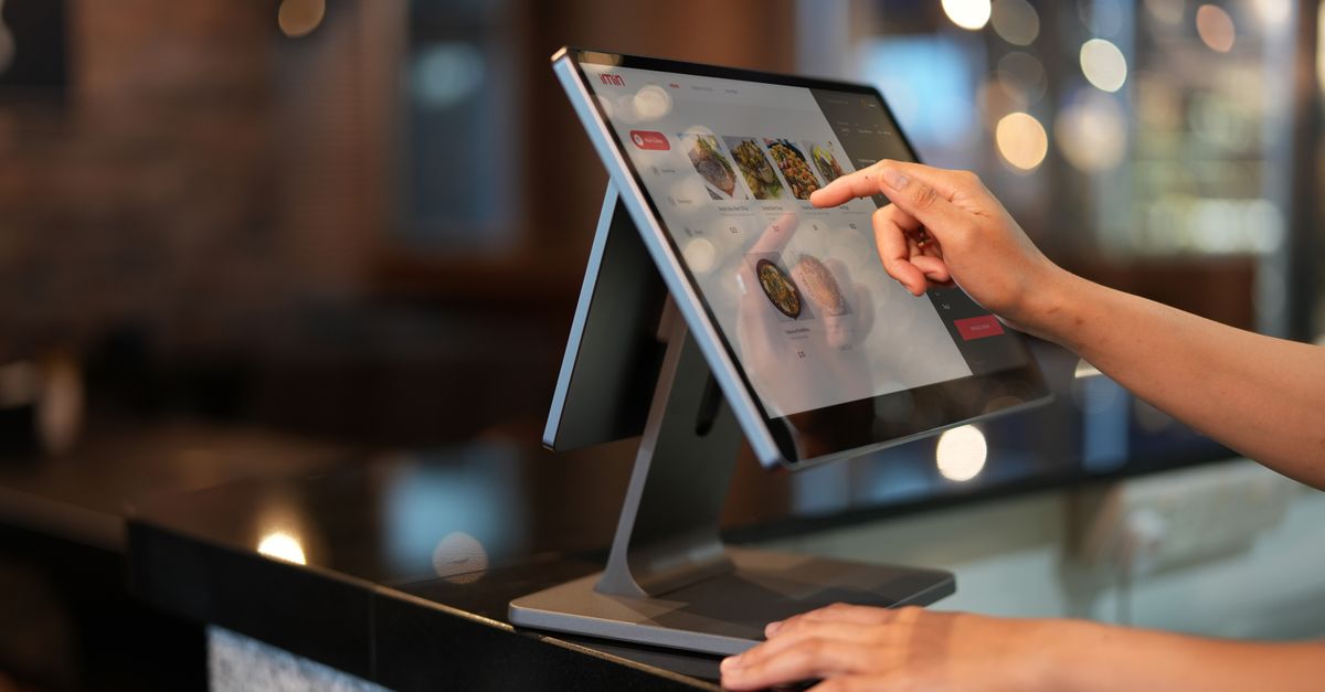 Close-up of a hand interacting with a touchscreen POS system in a restaurant setting.