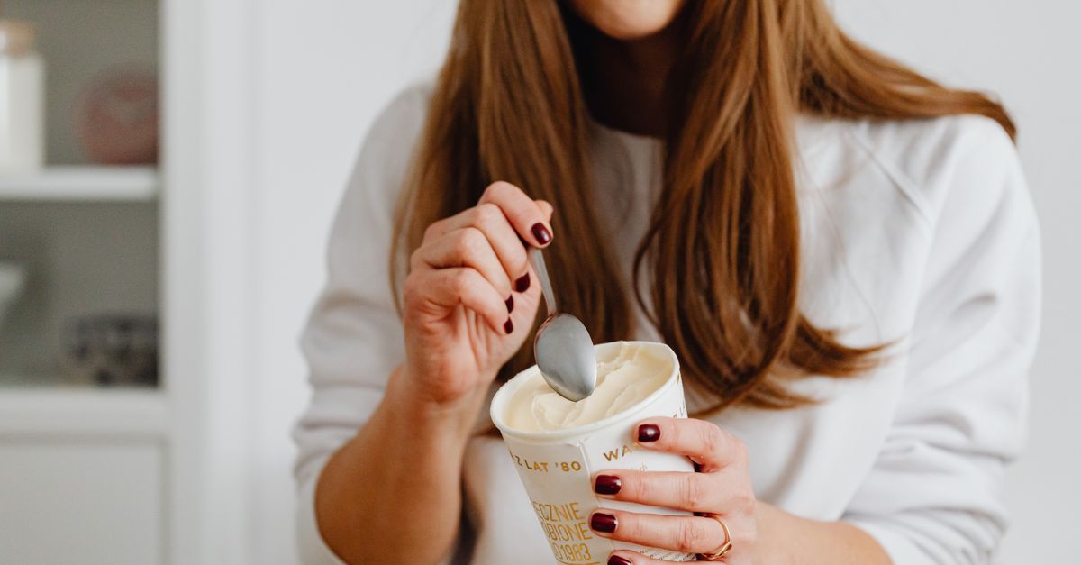A woman with red nail polish enjoying a cup of ice cream indoors, using a spoon.