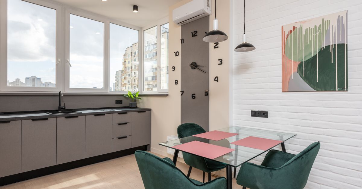 Interior of light kitchen with dining zone furnished with wooden counter and glass dinner table with soft chairs with brick white wall and wooden floor