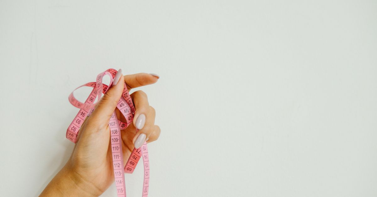 A woman's hand holds a pink measuring tape against a plain background, offering ample copy space.