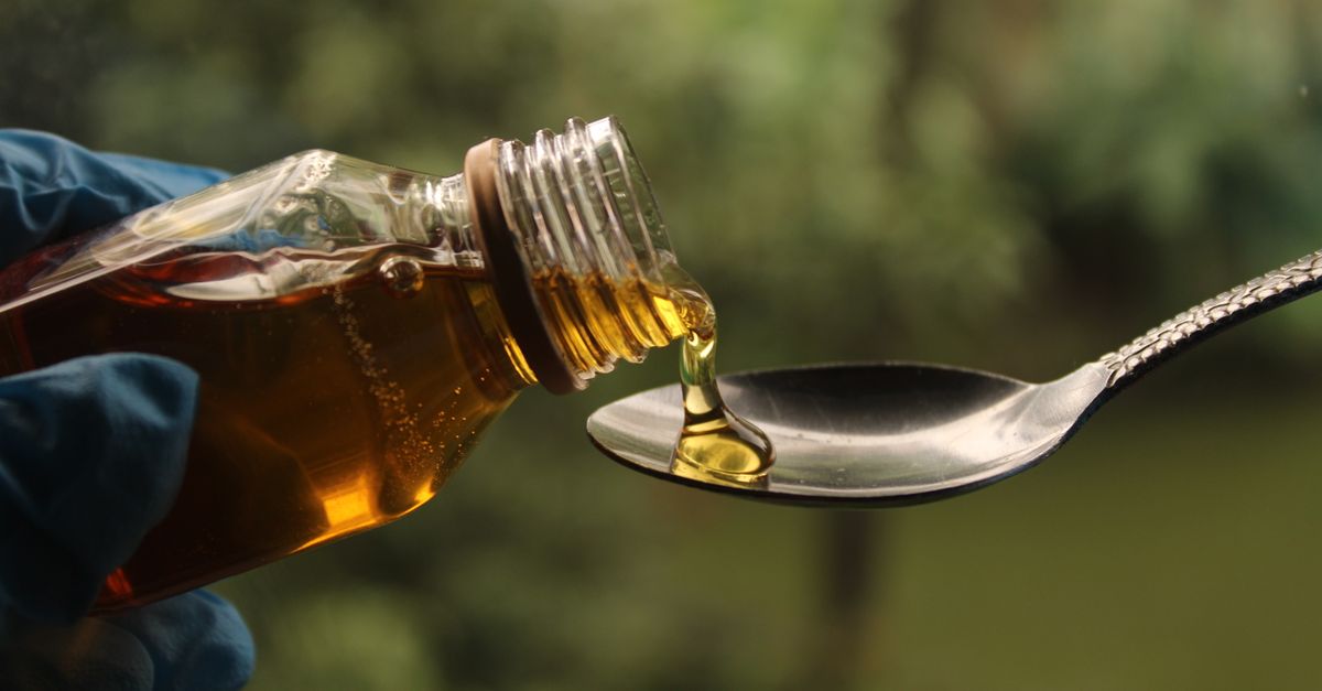Close-up of golden liquid being poured from bottle into spoon against blurred background.