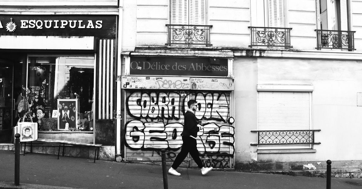 Monochrome image of a street with graffiti art and a person walking in Paris.
