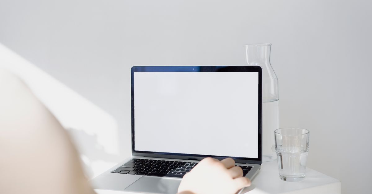 A minimalistic setup featuring a blank laptop screen, glass of water, and jug on a bright workspace.