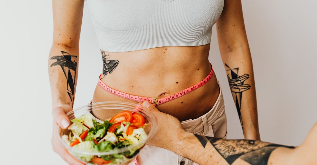 Fit woman measuring waist while holding a healthy salad bowl